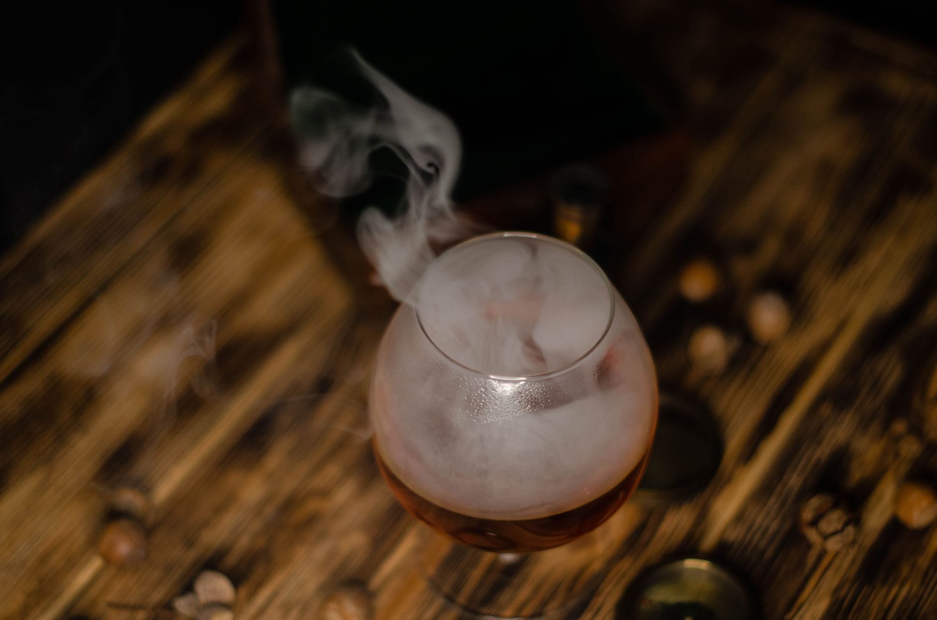 Smoke rising from a smoked bourbon old fashioned on dark wood