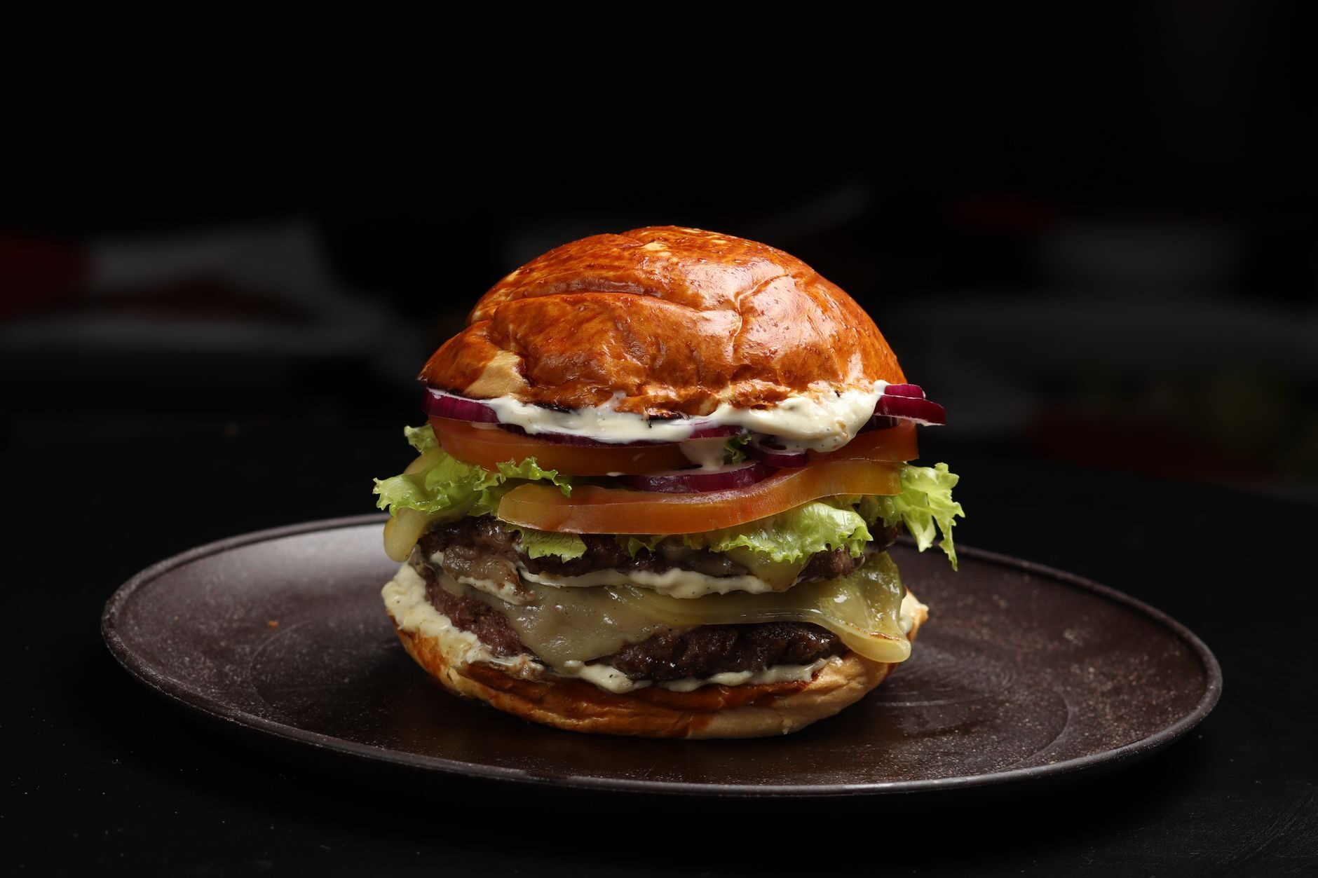A dry-aged style burger on a dark ceramic plate lit by a single warm source