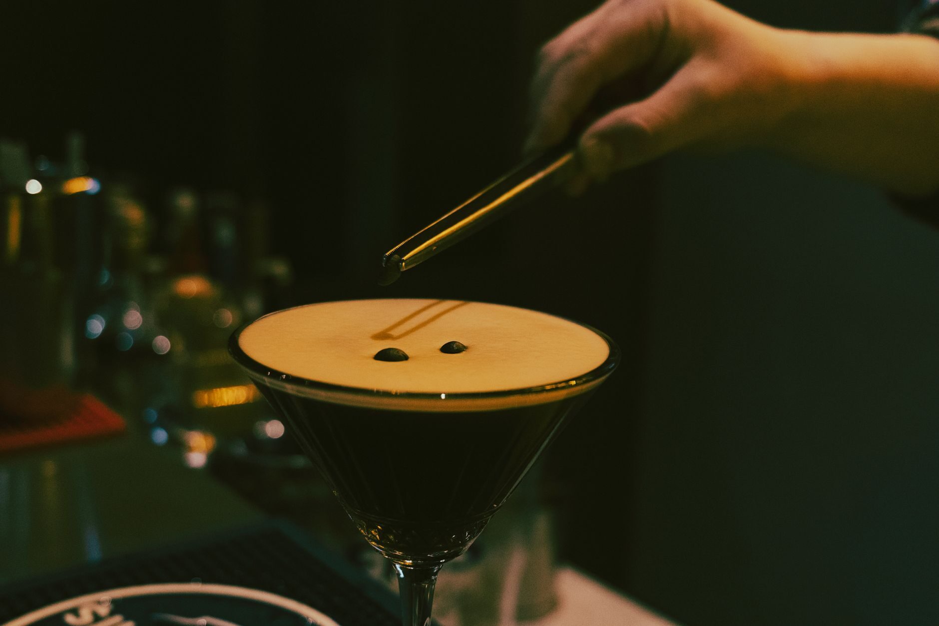 A bartender setting coffee beans onto a foamed espresso martini at a dark bar