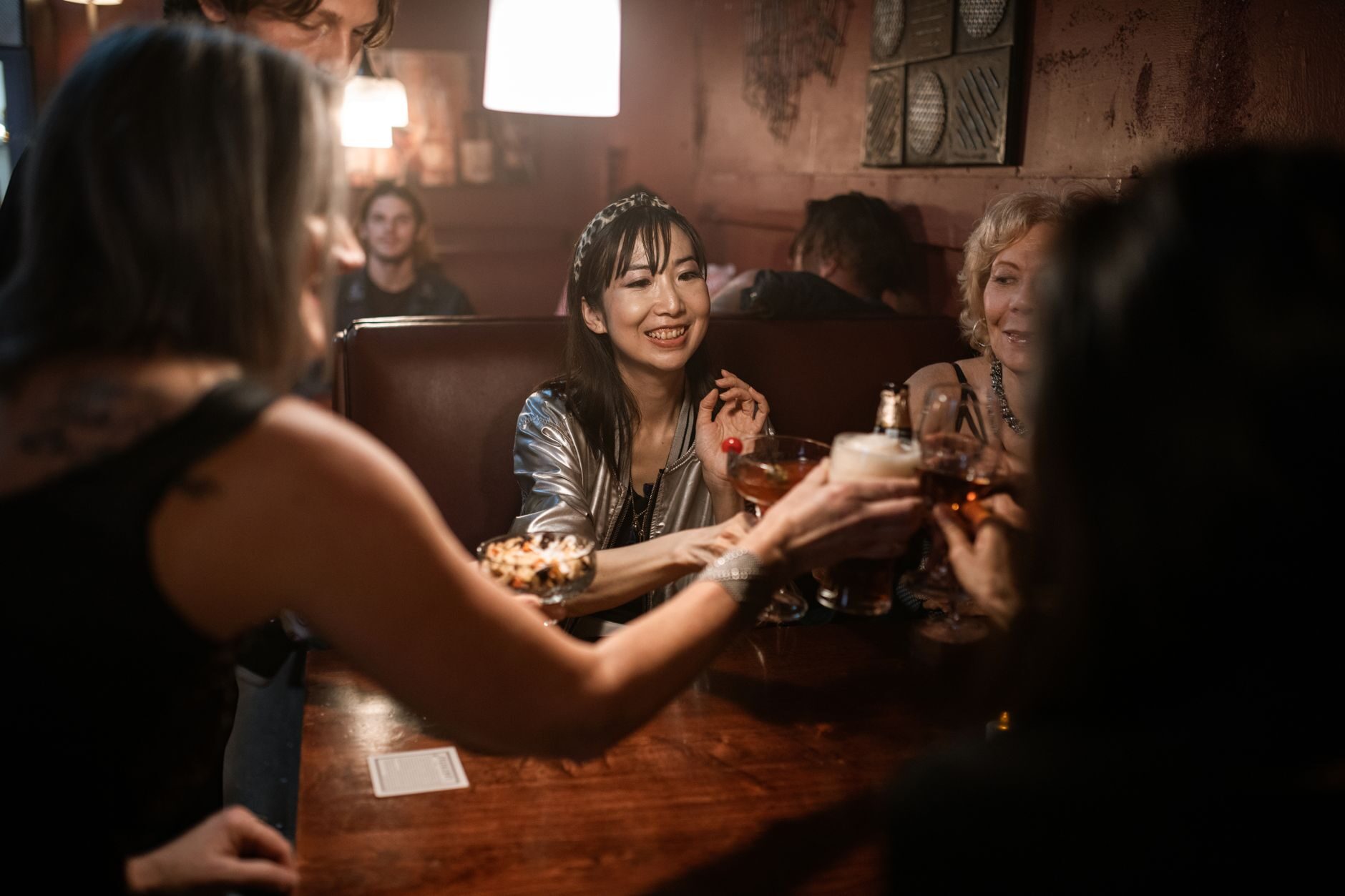 Three friends laughing in a dark tufted booth under warm amber light