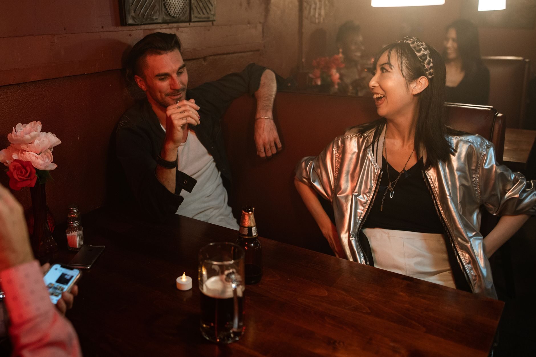 A couple in intimate conversation in a dark red booth over cocktails